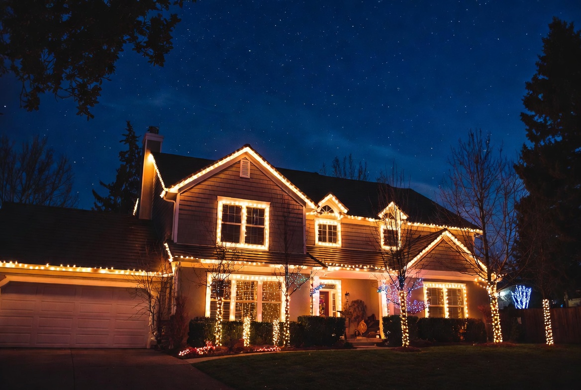 Two-story suburban home with elegant warm white Christmas lights outlining roof, windows and trees